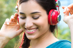 A teenage girl listening to music with headphones and smiling with a virtually clear Invisalign for Teen aligner tray